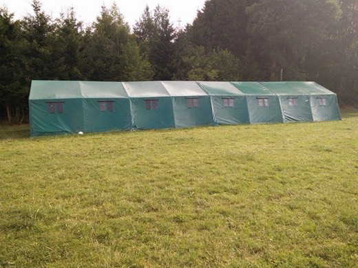 De tent Bink in volle lengte op een kampweide aan de bosrand.